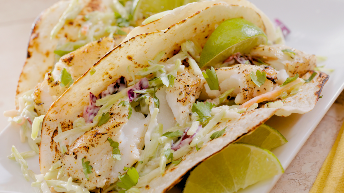 Picture of a white fish taco, with slaw and lime wedges.