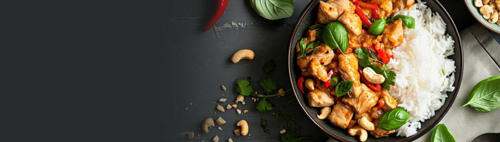 A bowl of rice, chicken and vegetables topped with cashews and basil leaves, on a dark background.